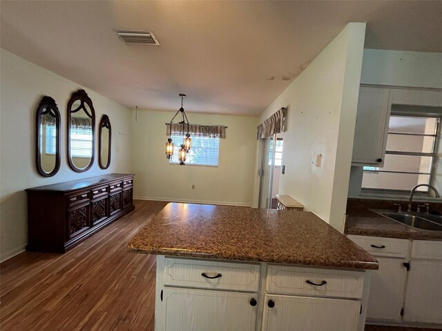 kitchen featuring white cabinets, hanging light fixtures, an inviting chandelier, sink, and wood-type flooring