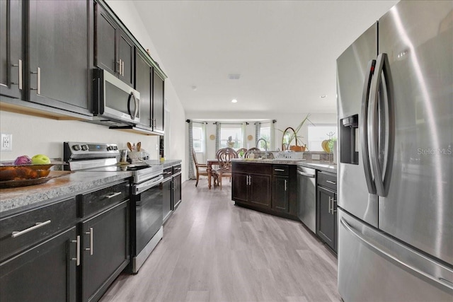 kitchen with light wood-type flooring, stainless steel appliances, dark brown cabinetry, and light stone counters