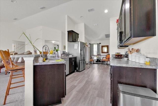 kitchen with dark brown cabinetry, a breakfast bar, appliances with stainless steel finishes, and light hardwood / wood-style floors