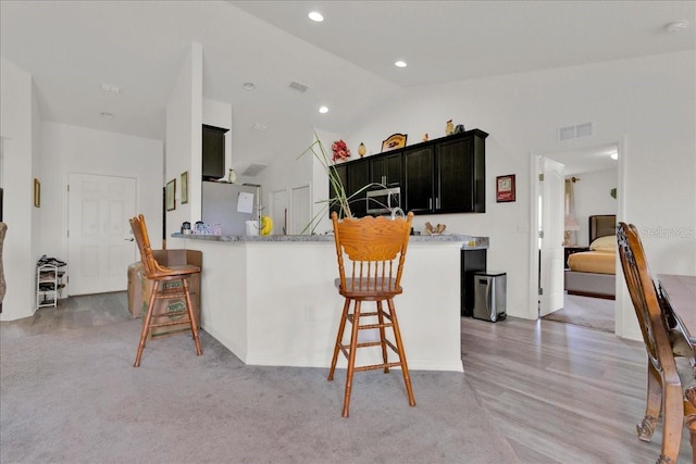 kitchen featuring a breakfast bar, lofted ceiling, kitchen peninsula, and light hardwood / wood-style floors