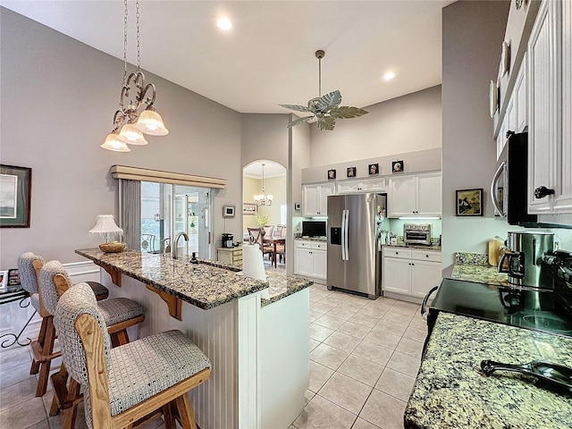 kitchen featuring stainless steel appliances, light tile patterned floors, white cabinets, a high ceiling, and decorative light fixtures