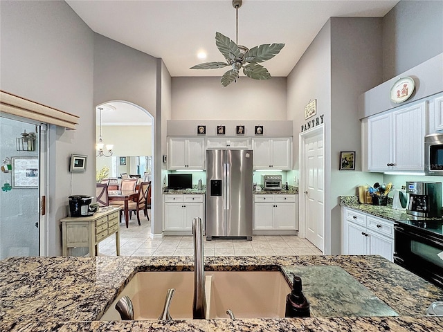 kitchen featuring stainless steel appliances, a towering ceiling, white cabinetry, and light tile patterned floors