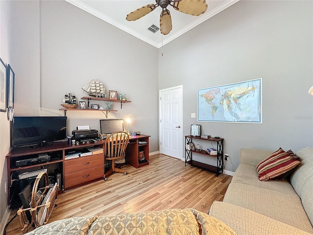 office space with ceiling fan, light hardwood / wood-style flooring, ornamental molding, and a towering ceiling