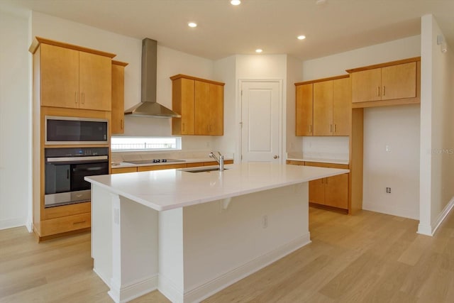 kitchen featuring built in microwave, sink, an island with sink, oven, and wall chimney range hood