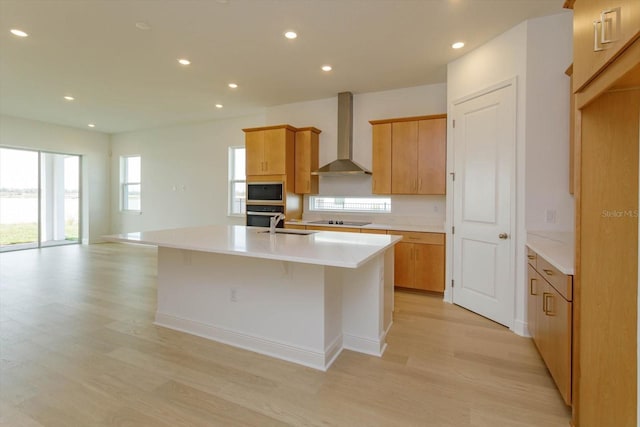 kitchen with built in microwave, a kitchen island with sink, stainless steel oven, black electric stovetop, and wall chimney exhaust hood