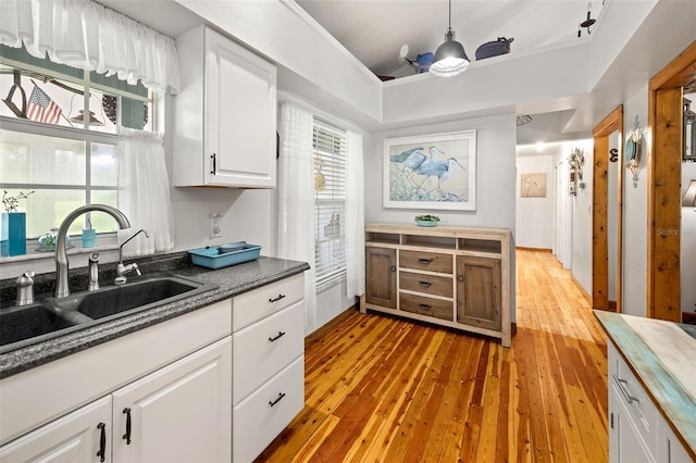 kitchen with sink, decorative light fixtures, white cabinets, and light wood-type flooring