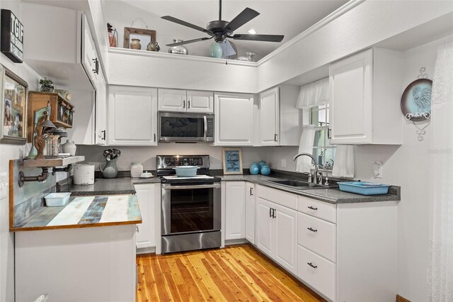 kitchen featuring appliances with stainless steel finishes, white cabinetry, a sink, and light wood finished floors