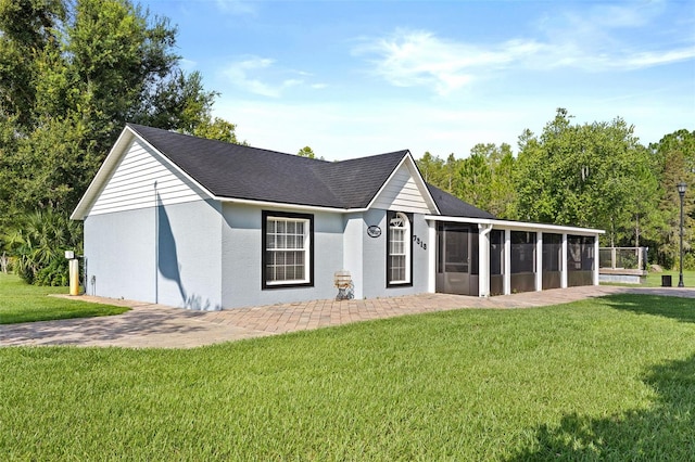 view of front of property with roof with shingles, a front yard, a sunroom, and stucco siding