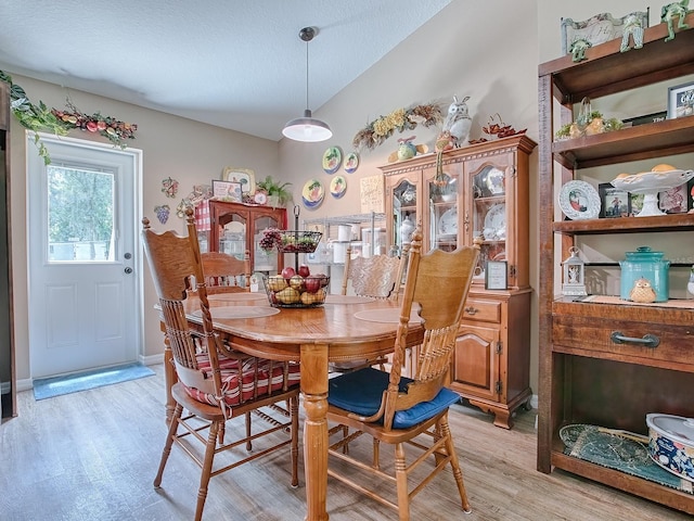 dining area with lofted ceiling, a textured ceiling, and light hardwood / wood-style floors