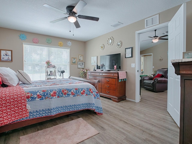 bedroom featuring ceiling fan, light wood-type flooring, a textured ceiling, and lofted ceiling