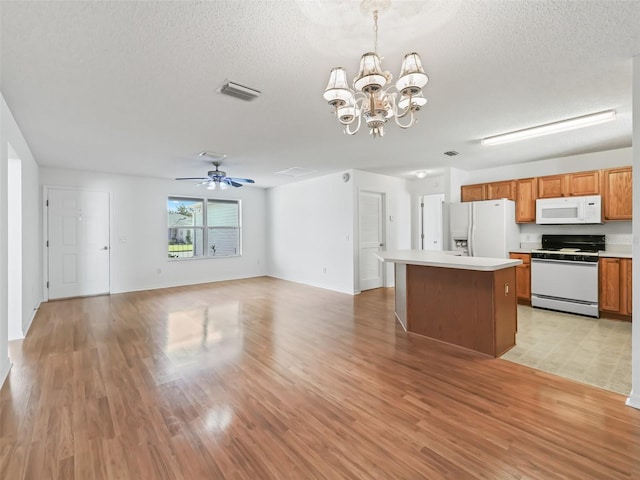 kitchen featuring light hardwood / wood-style flooring, a textured ceiling, ceiling fan with notable chandelier, a kitchen island, and white appliances