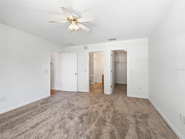 unfurnished bedroom with a walk in closet, a closet, a textured ceiling, ceiling fan, and light colored carpet