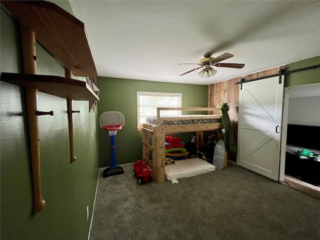 bedroom featuring ceiling fan, a barn door, and dark colored carpet