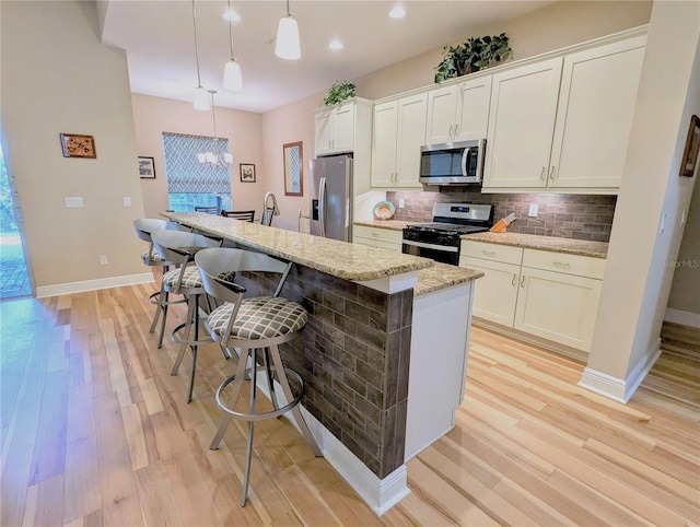 kitchen featuring appliances with stainless steel finishes, a breakfast bar, a kitchen island with sink, and pendant lighting