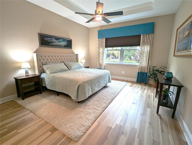 bedroom featuring light hardwood / wood-style floors, a raised ceiling, crown molding, and ceiling fan