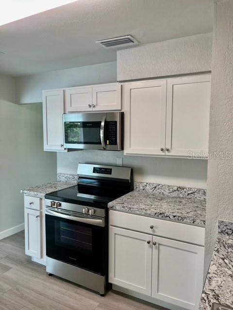 kitchen featuring appliances with stainless steel finishes, white cabinetry, light stone countertops, and light hardwood / wood-style floors