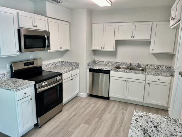 kitchen with light hardwood / wood-style flooring, white cabinetry, appliances with stainless steel finishes, light stone countertops, and sink