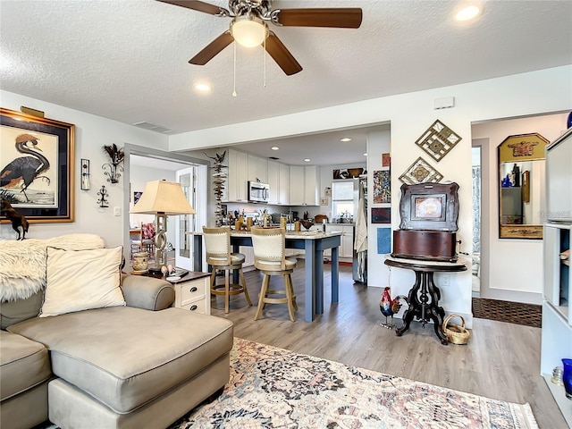 living room featuring a textured ceiling, ceiling fan, and light hardwood / wood-style floors