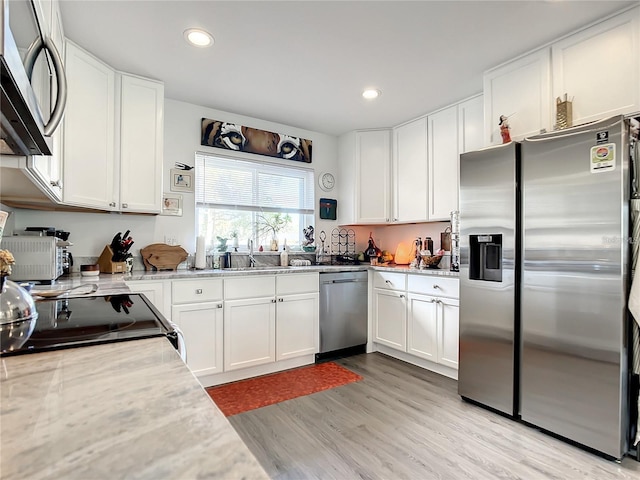 kitchen featuring appliances with stainless steel finishes, light wood-type flooring, light stone counters, and white cabinetry