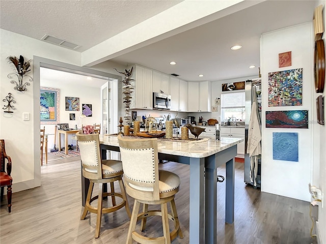 kitchen featuring a textured ceiling, light hardwood / wood-style floors, light stone countertops, white cabinets, and a kitchen bar