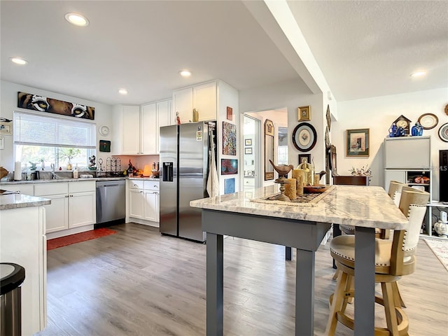 kitchen featuring light hardwood / wood-style flooring, white cabinets, stainless steel appliances, and light stone counters