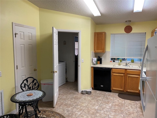 kitchen featuring sink, black dishwasher, stainless steel fridge, a textured ceiling, and light tile patterned floors