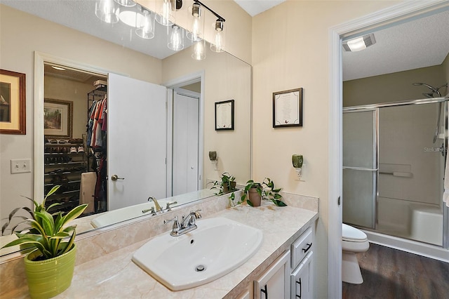 bathroom with a textured ceiling, a shower with door, toilet, hardwood / wood-style flooring, and vanity