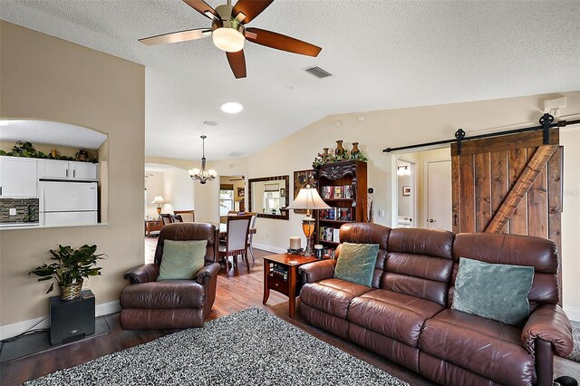 living room with ceiling fan with notable chandelier, a textured ceiling, hardwood / wood-style floors, lofted ceiling, and a barn door