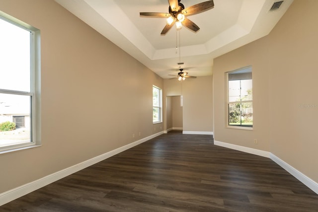 unfurnished room featuring a tray ceiling, a wealth of natural light, ceiling fan, and dark hardwood / wood-style floors