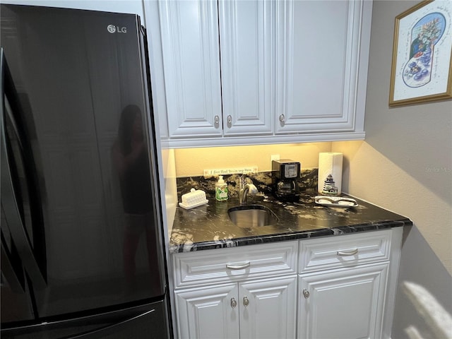 bar featuring refrigerator, dark stone counters, white cabinetry, and sink