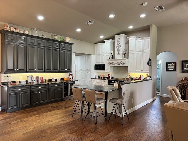 kitchen with white cabinets, black microwave, dark hardwood / wood-style flooring, lofted ceiling, and a breakfast bar area