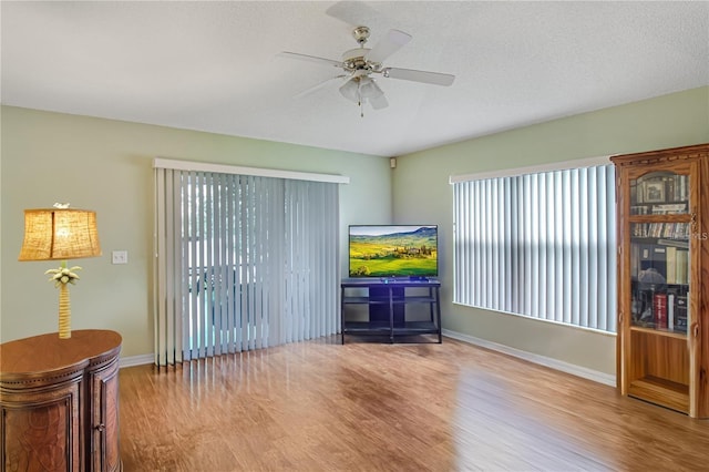 living area featuring a ceiling fan, wood finished floors, baseboards, and a textured ceiling