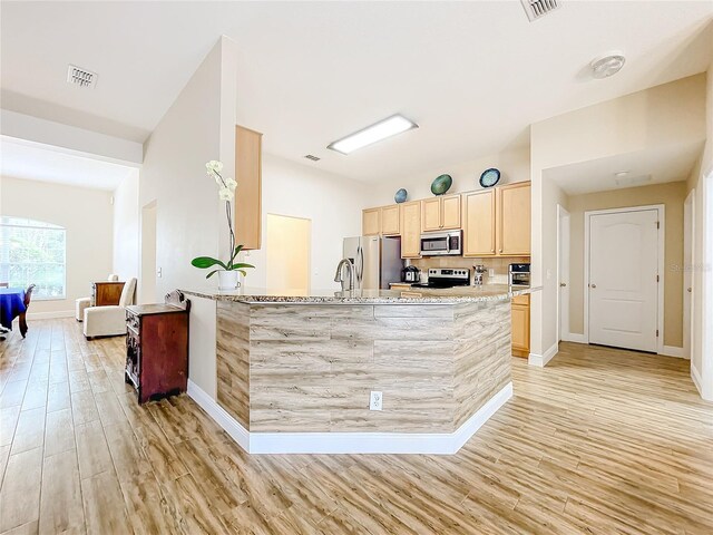 kitchen featuring light wood-type flooring, light stone counters, stainless steel appliances, light brown cabinets, and kitchen peninsula