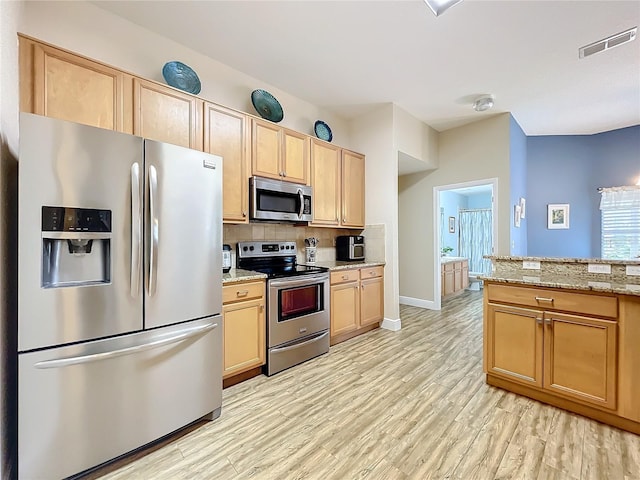 kitchen featuring decorative backsplash, light stone countertops, appliances with stainless steel finishes, light brown cabinets, and light hardwood / wood-style floors