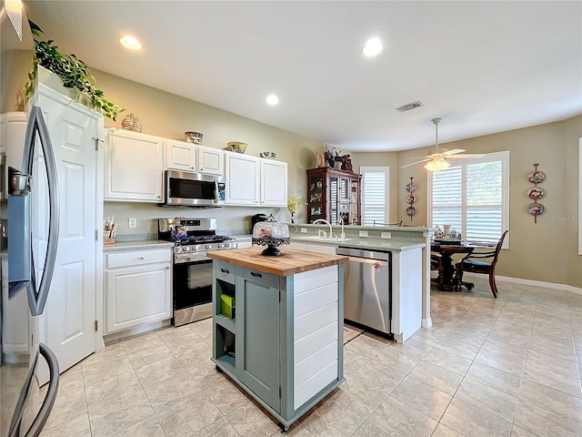 kitchen featuring white cabinetry, wooden counters, kitchen peninsula, a kitchen island, and appliances with stainless steel finishes