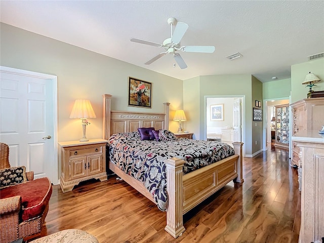 bedroom with a textured ceiling, hardwood / wood-style flooring, connected bathroom, and ceiling fan