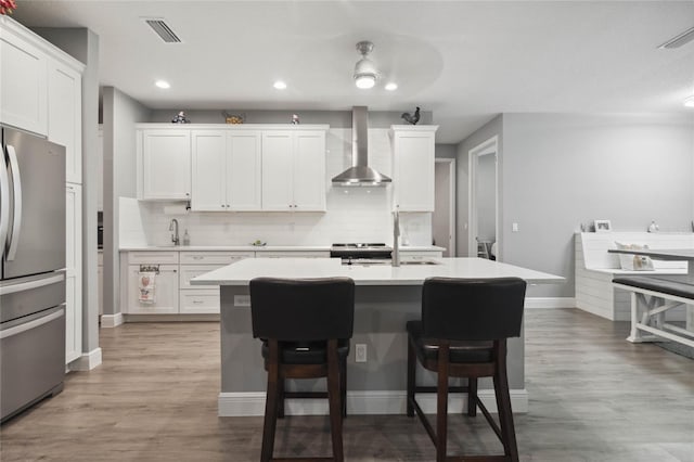 kitchen with white cabinets, backsplash, light hardwood / wood-style flooring, appliances with stainless steel finishes, and wall chimney range hood