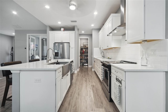 kitchen with light hardwood / wood-style floors, stainless steel appliances, decorative backsplash, and wall chimney range hood