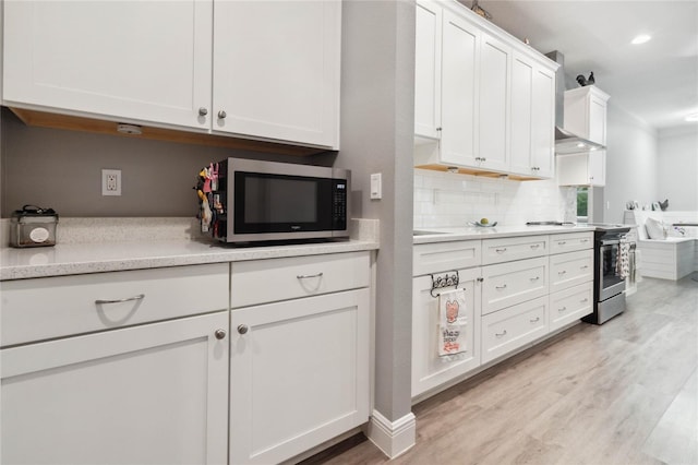 kitchen featuring appliances with stainless steel finishes, light hardwood / wood-style floors, white cabinetry, wall chimney range hood, and tasteful backsplash