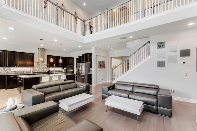 living room with a high ceiling, sink, and light wood-type flooring