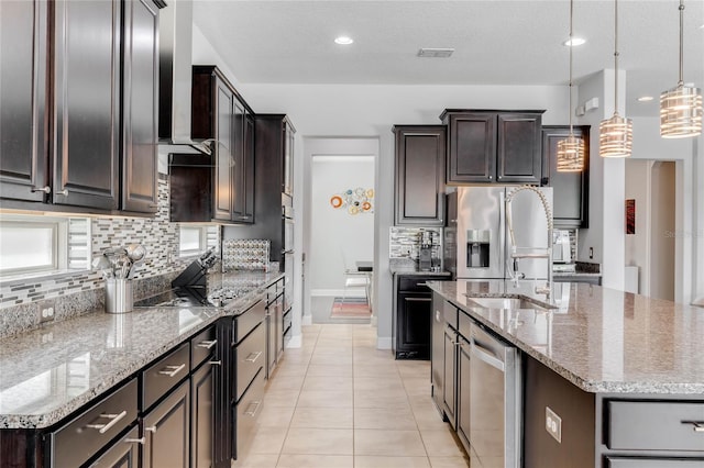 kitchen featuring light tile patterned floors, appliances with stainless steel finishes, a kitchen island with sink, and decorative light fixtures