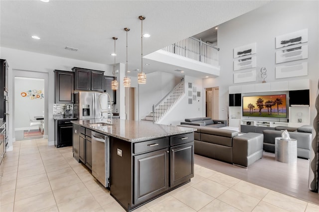 kitchen featuring hanging light fixtures, a kitchen island with sink, appliances with stainless steel finishes, light stone countertops, and light tile patterned floors