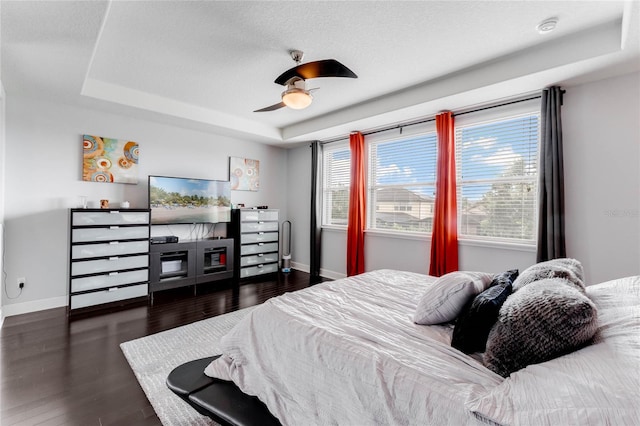 bedroom with ceiling fan, a tray ceiling, and dark wood-type flooring