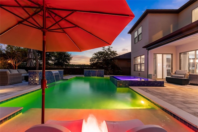 pool at dusk with outdoor lounge area, pool water feature, an in ground hot tub, and a patio area