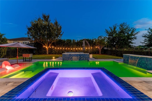 pool at dusk with an in ground hot tub, pool water feature, and a patio