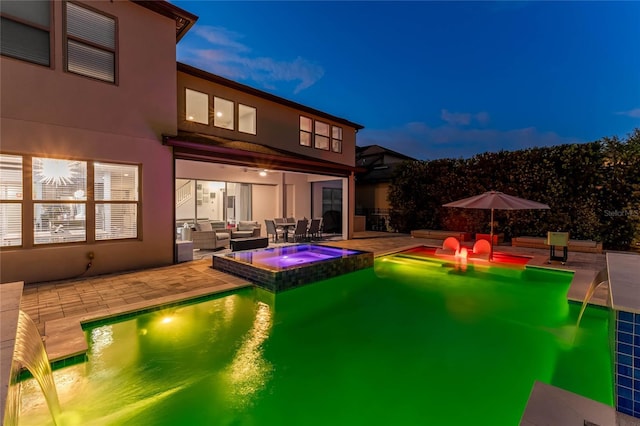 back house at dusk featuring an in ground hot tub, a patio, and an outdoor living space with a fire pit