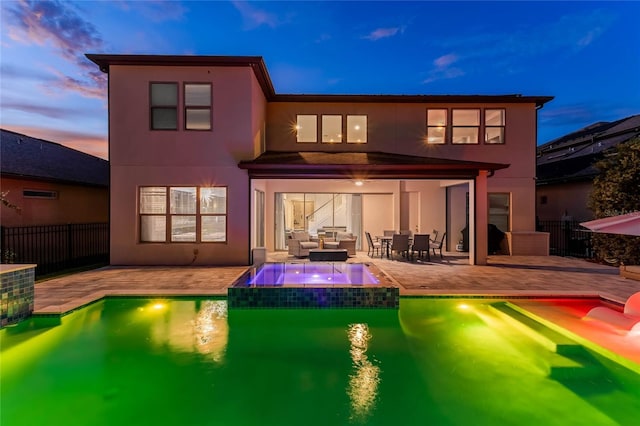 back house at dusk with a swimming pool with hot tub, outdoor lounge area, and a patio area