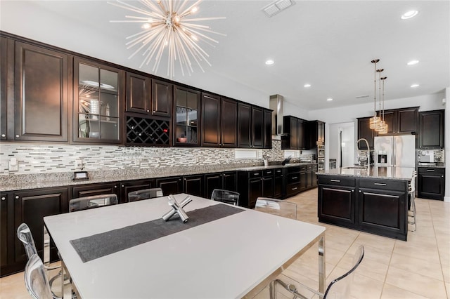 kitchen featuring sink, stainless steel fridge, a kitchen island with sink, dark brown cabinetry, and decorative light fixtures