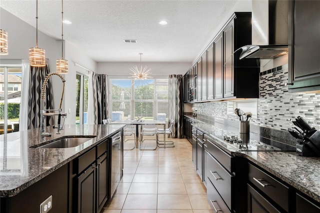 kitchen with dark brown cabinets, dishwasher, pendant lighting, dark stone counters, and wall chimney range hood