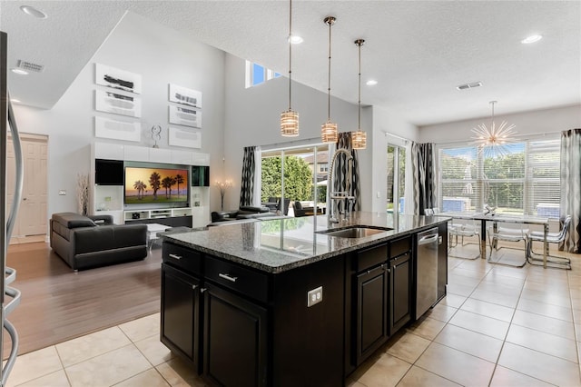 kitchen featuring dark stone countertops, light wood-type flooring, a kitchen island with sink, dishwasher, and hanging light fixtures